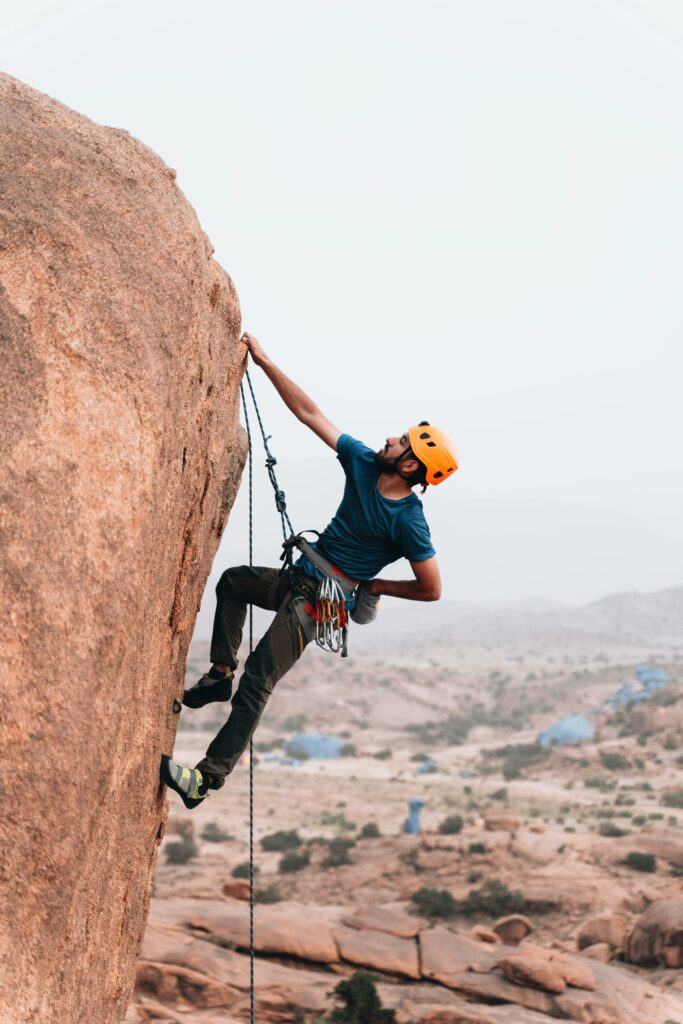 A man in a helmet rock climbing a steep cliff outdoors, showcasing adventure and skill.